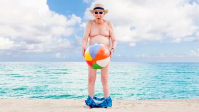 A humorous photo of an older man holding a beach ball in front of him. His swimsuit is around his ankles.